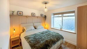 Een slaapkamer met een bed, nachtkastjes, een raam met uitzicht en een hanglamp.
