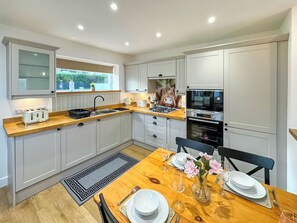 Une cuisine moderne avec des meubles gris, un plan de travail en bois, un four encastré et un coin repas avec une table dressée pour deux personnes.