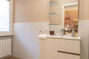 Une salle de bain avec une fenêtre, un radiateur, un lavabo avec un miroir et une serviette posée sur le comptoir.