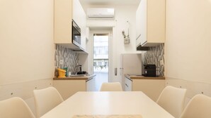 Una cocina moderna con una isla central, armarios blancos y vistas a través de una puerta abierta.