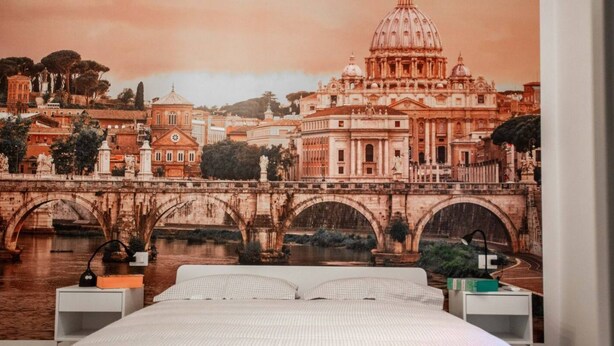 Un dormitorio con una cama grande, una mesita de noche, una lámpara y un mural en la pared con una vista urbana.