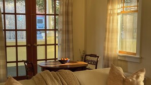 Una sala de estar acogedora con un sofá, una mesa con un frutero y vistas al exterior a través de ventanas amplias.