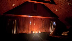 Interior acogedor de una cabaña con techo inclinado, paredes de madera, chimenea y una cama.