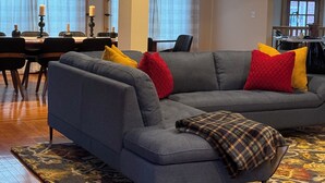 Una sala de estar moderna con un sofá seccional gris, un tapete estampado y un comedor con mesa y sillas.