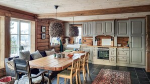 Une cuisine chaleureuse, aménagée dans le style d’un chalet, avec des murs en bois, une table à manger entourée de chaises et une grande fenêtre offrant une vue sur l’extérieur.