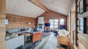 L’intérieur chaleureux d’un chalet en bois comprend un canapé, un fauteuil à bascule en bois, un téléviseur et une cheminée.