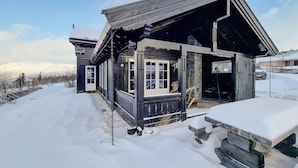 Une cabane en bois dotée d’un porche et d’un auvent, entourée de neige.