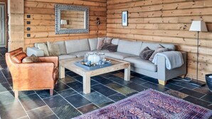 L'intérieur d'un chalet confortable, avec un canapé gris, un fauteuil en cuir marron, une table basse agrémentée d'objets décoratifs et un tapis à motifs.