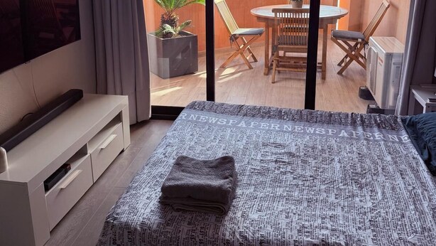 Habitación de hotel con cama, televisor, balcón con mesa y sillas, y vista al mar.