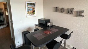 Una cocina moderna con una mesa de comedor, taburetes de bar, un microondas y un tostador. Un cartel con la palabra 'HOME' está en la pared, y una fotografía enmarcada de Cannes se encuentra sobre la encimera.