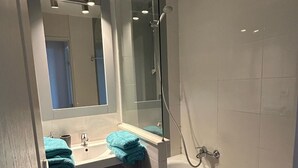Un baño con ducha envuelta en cristal, lavabo con espejo y bañera.