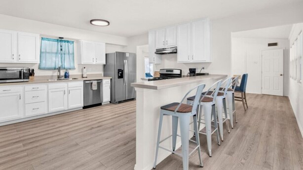 Una cocina moderna con armarios blancos, electrodomésticos de acero inoxidable y una zona de bar con taburetes.