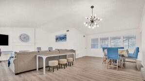 Una habitación amplia con suelo de madera, un sofá blanco, una mesa de comedor con sillas y un ventanal grande.