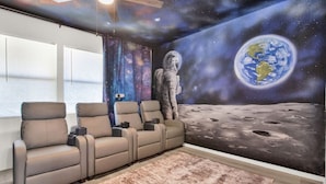 Una habitación con un mural alusivo al espacio, sillones reclinables y un gran ventanal.
