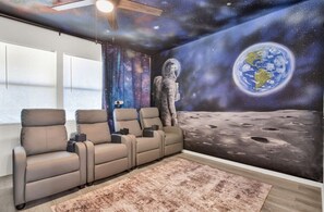 Una habitación con un mural alusivo al espacio, sillones reclinables y un gran ventanal.