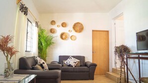 Ein Wohnzimmer mit zwei Sofas, einer großen Grünpflanze und dekorativen Gewebearbeiten an der Wand.