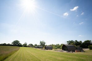 Eine Reihe Holzhütten mit Picknicktischen in einem grünen Feld unter blauem Himmel.