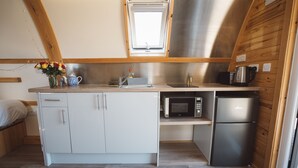 Una cucina compatta con mobili bianchi, un forno a microonde, un frigorifero, un lavello e una finestra sopra il lavello.