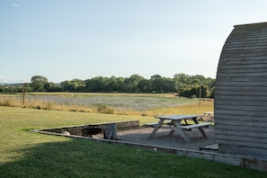 Un área de picnic con una mesa y bancos de madera, rodeada por un campo cubierto de hierba y un edificio de madera.