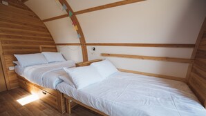Un lit simple avec un cadre en bois et une literie blanche, dans une pièce aux murs en bois et au plafond voûté.