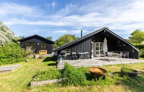 A black wooden cabin with a deck, outdoor seating, and a fire pit.