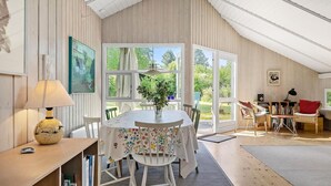 Una habitación acogedora con detalles de madera, una mesa de comedor con sillas, una estantería y una ventana con cortinas.
