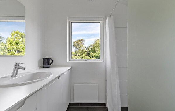 A bathroom with a white sink, a mirror, a window with a view of trees, and a shower curtain.