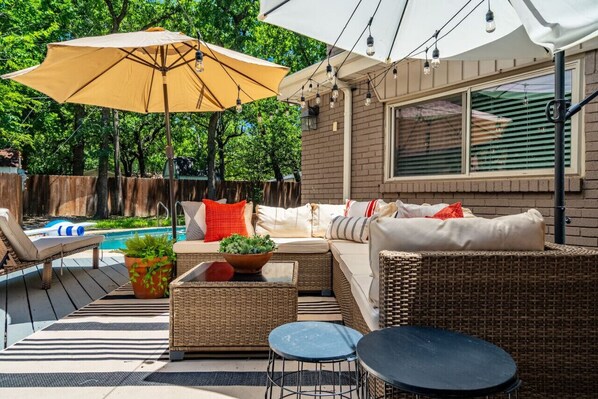 A patio area with wicker furniture, a pool, and a large umbrella.