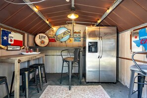 A compact kitchen with a stainless steel refrigerator, a bar area with stools, and vintage decor including a 'Blue Moon' sign and a Texas flag.