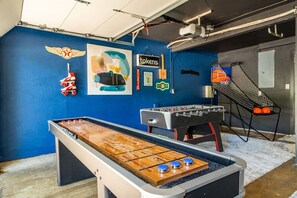 A room with a foosball table, a pool table, and a basketball hoop.