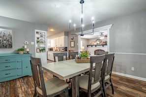 A dining area with a light-colored table and dark wooden chairs, a teal cabinet, and a chandelier.