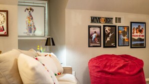 A cozy living room with a beige sofa, a red bean bag, and a wall decorated with movie posters.