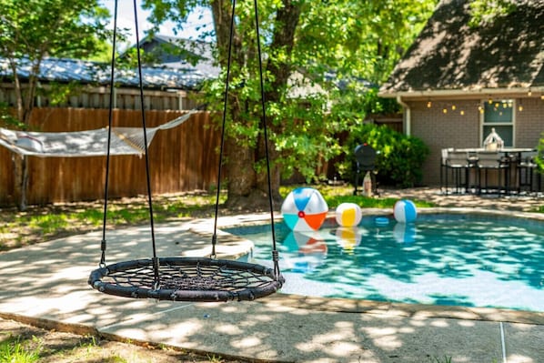 A backyard with a pool, a hammock, and a swing set.