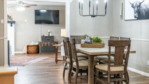 A dining area with a wooden table and chairs, a chandelier, and a mounted TV.