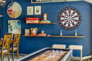 A room with a dartboard, shelves with snacks, and a table with a board game. - Pool House w/ Outdoor Bar, Game Room & Movie Room (Irving)