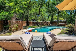 A backyard with a swimming pool, lounge chairs, and a wooden fence.