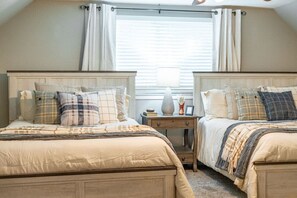 A bedroom with two beds, a nightstand, and a window with curtains.