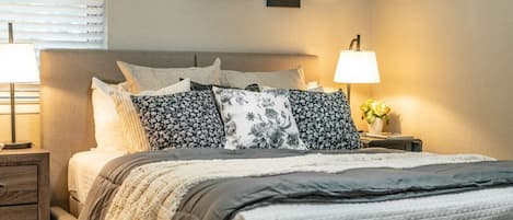 A neatly made bed with floral-patterned pillows, a bedside lamp, and a small plant on the nightstand.