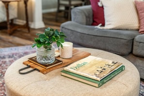 A round ottoman with a book titled 'Dallas' and a small potted plant on top.