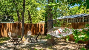 A backyard with a wooden fence, a hammock, and three Adirondack chairs around a fire pit.