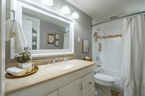 A bathroom with a large mirror, white sink, and bathtub.