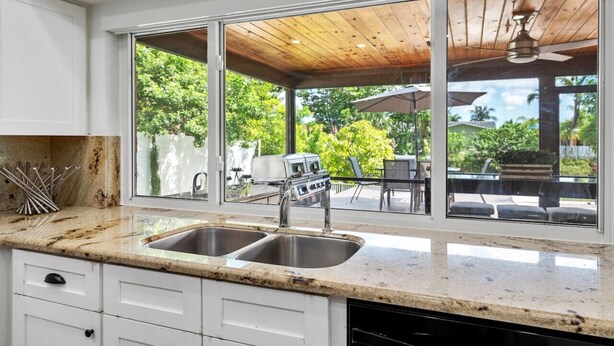 A kitchen with a large window, a built-in grill, and a view of an outdoor patio. - BBQs & Breezes: Waterfront Pool House Escape (Margate)
