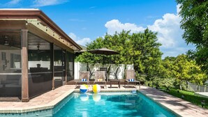 A swimming pool with lounge chairs and umbrellas, surrounded by trees and a fence. - BBQs & Breezes: Waterfront Pool House Escape (Margate)