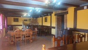 A dining area with wooden tables and chairs, a brick fireplace, and a tiled floor.