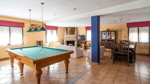 A pool table in a room with a fireplace, a dining area, and a large window.