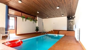 An indoor swimming pool with a wooden ceiling, a red inflatable ring, and a potted plant.