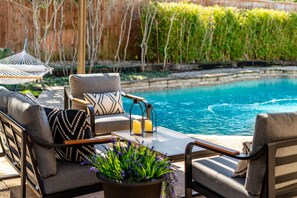 A poolside seating area with a sofa and chairs, a table with candles, and a view of the pool.