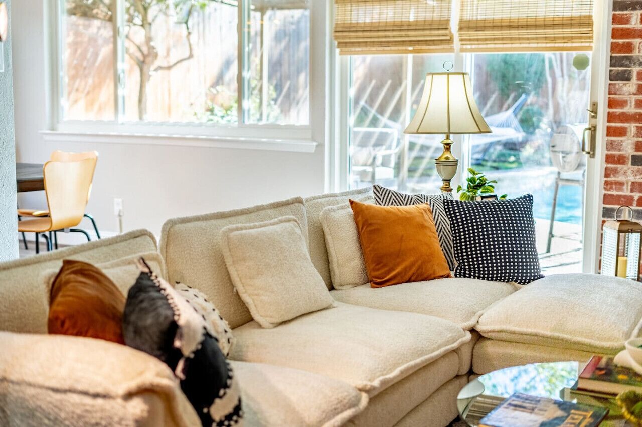 A cozy living room with a beige sectional sofa, a lamp, and a view of the outdoors.