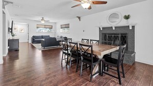 A spacious living area with a dining table, chairs, a fireplace, and a ceiling fan. - Tropical Pool w/ Tiki Bar, Fire Pit, Swing (Richardson)