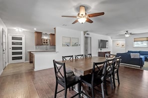 A modern kitchen with wooden cabinets, a dining area with a wooden table and chairs, and a living room with a blue sofa.